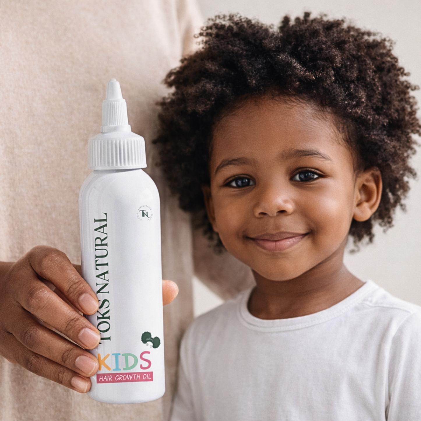 Child holding a bottle of YOKS NATURAL Kids Hair Growth Oil against a neutral background