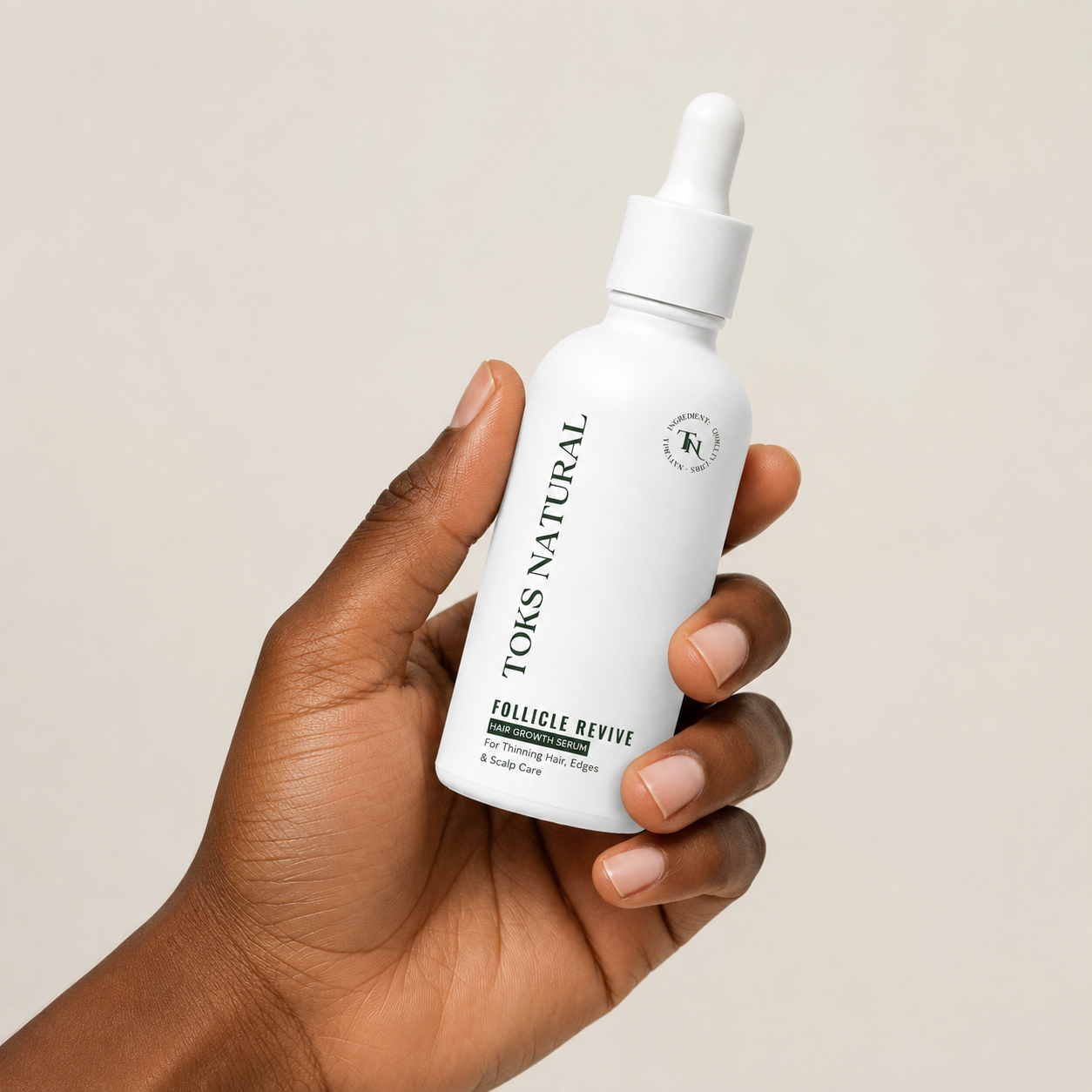 Hand holding a white bottle of TOKS NATURAL Follicle Revive on a beige background