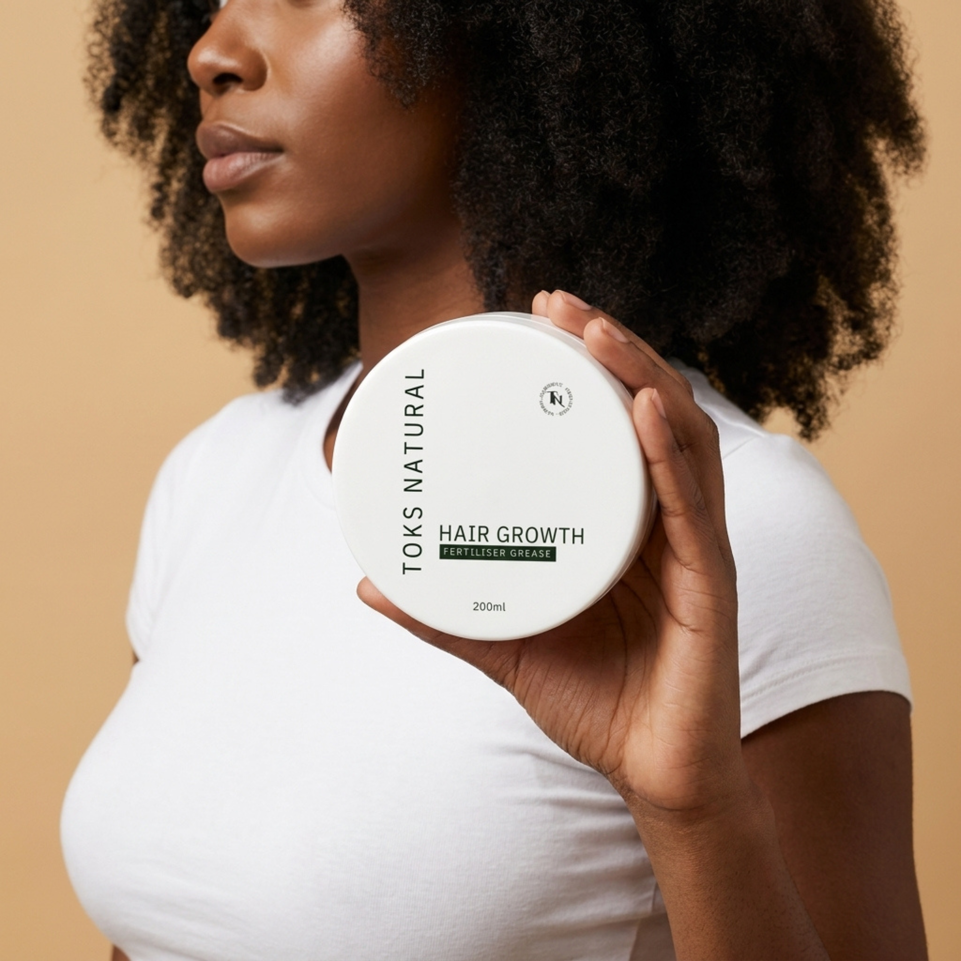 Woman holding a container of Toks Natural hair growth product against a beige background