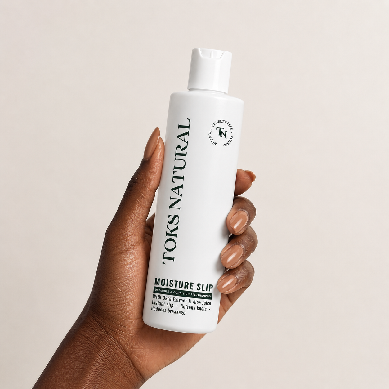 Hand holding a bottle of Toks Natural Moisture Slip against a beige background