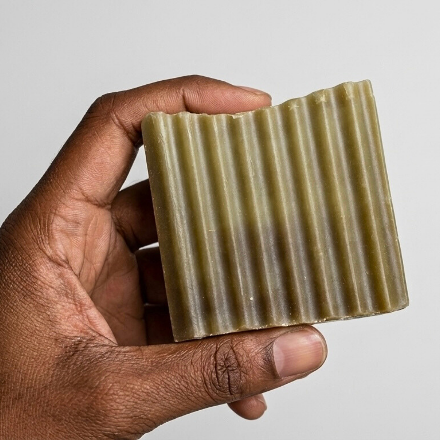 Hand holding a bar of soap with a ribbed texture against a plain background