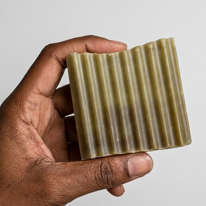 Hand holding a bar of soap with a ribbed texture against a plain background
