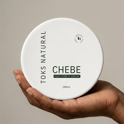 Hand holding a container of Toks Natural Chebe Hair Growth Grease against a beige background