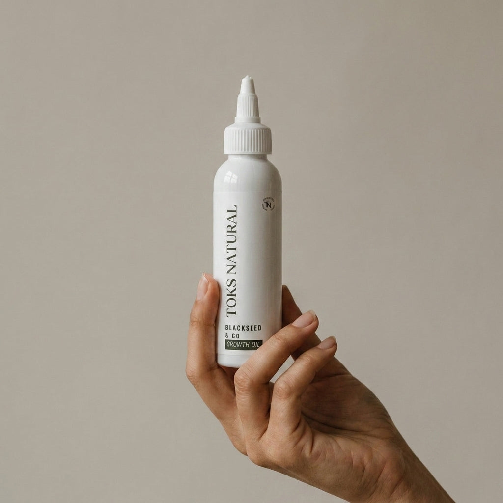 Hand holding a bottle of Tors Naturals Blackseed Growth Oil against a beige background