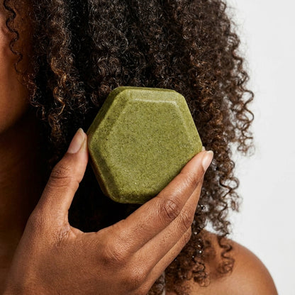 Person holding a green shampoo bar of soap close to their curly hair.