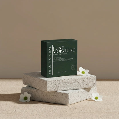Luxe Moisture shampoo bar soap packaging on a stone surface with flowers.