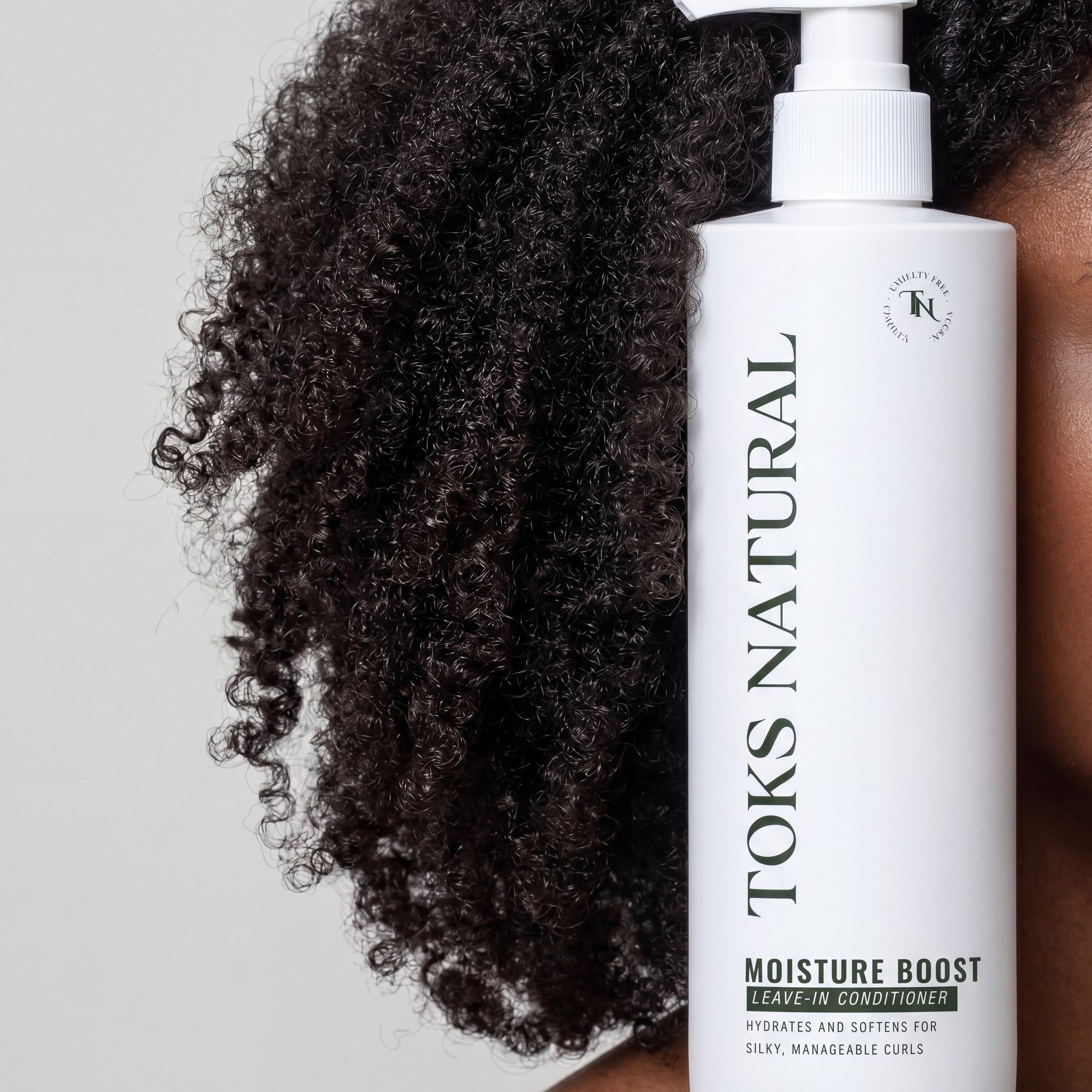 Toks Natural leave-in conditioner bottle with curly hair on a light gray background