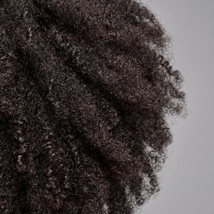 Close-up of a person with textured dark brown hair on a plain background