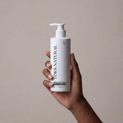Hand holding a bottle of Kevyn Aucoin Toms Natural product against a beige background