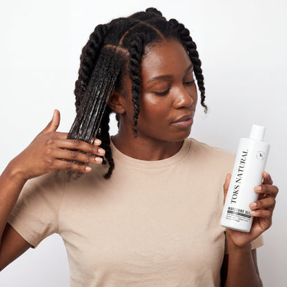 Woman with braided hair holding a bottle of Toks Natural product against a white background