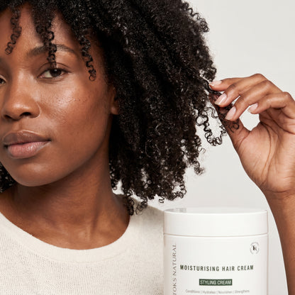 Woman with curly hair touching a container of Toks Natural Styling Cream on a neutral background