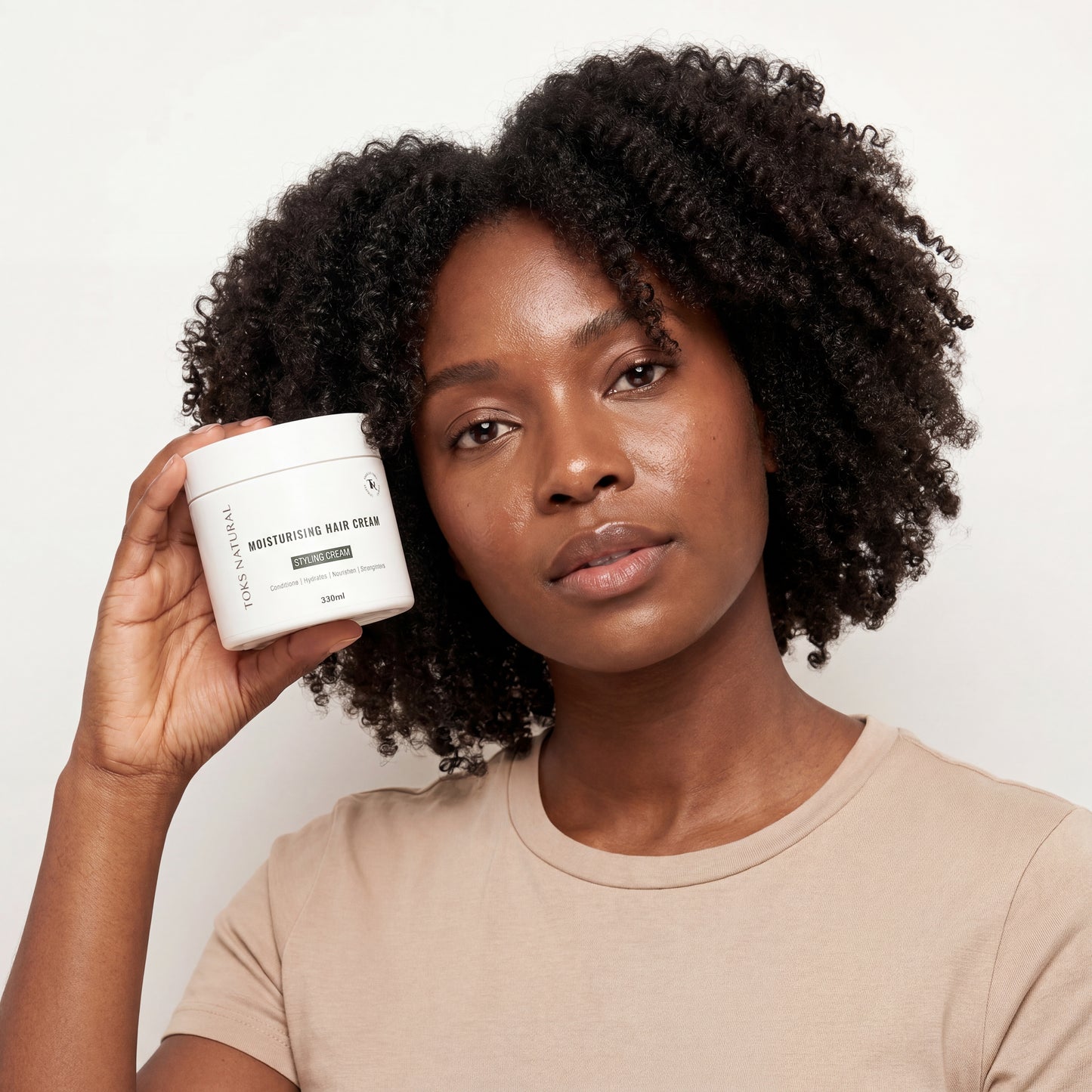 Woman holding a white container with text, wearing a beige shirt on a plain background