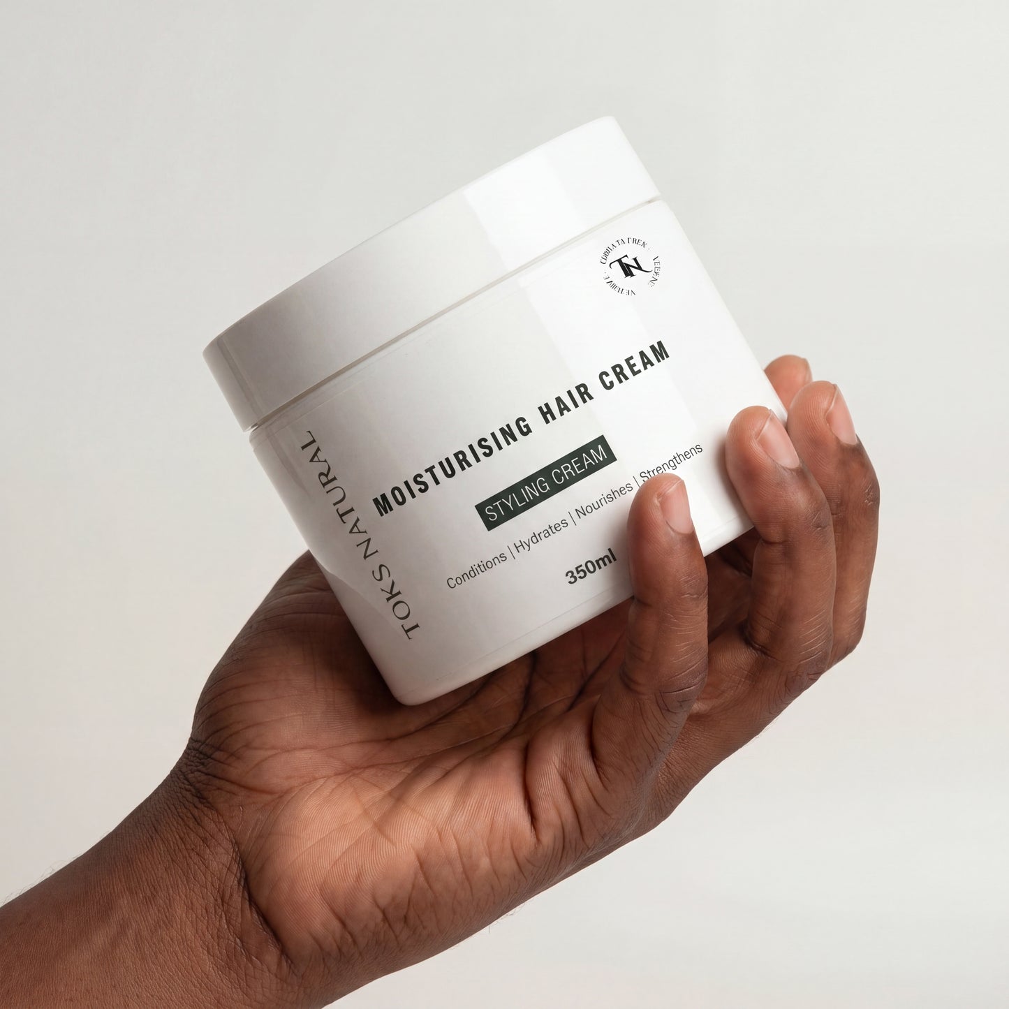 Hand holding a jar of Toks Natural Moisturising Hair Cream against a white background