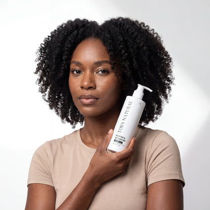 Woman holding a bottle of Tuku Natural hair care product against a white background