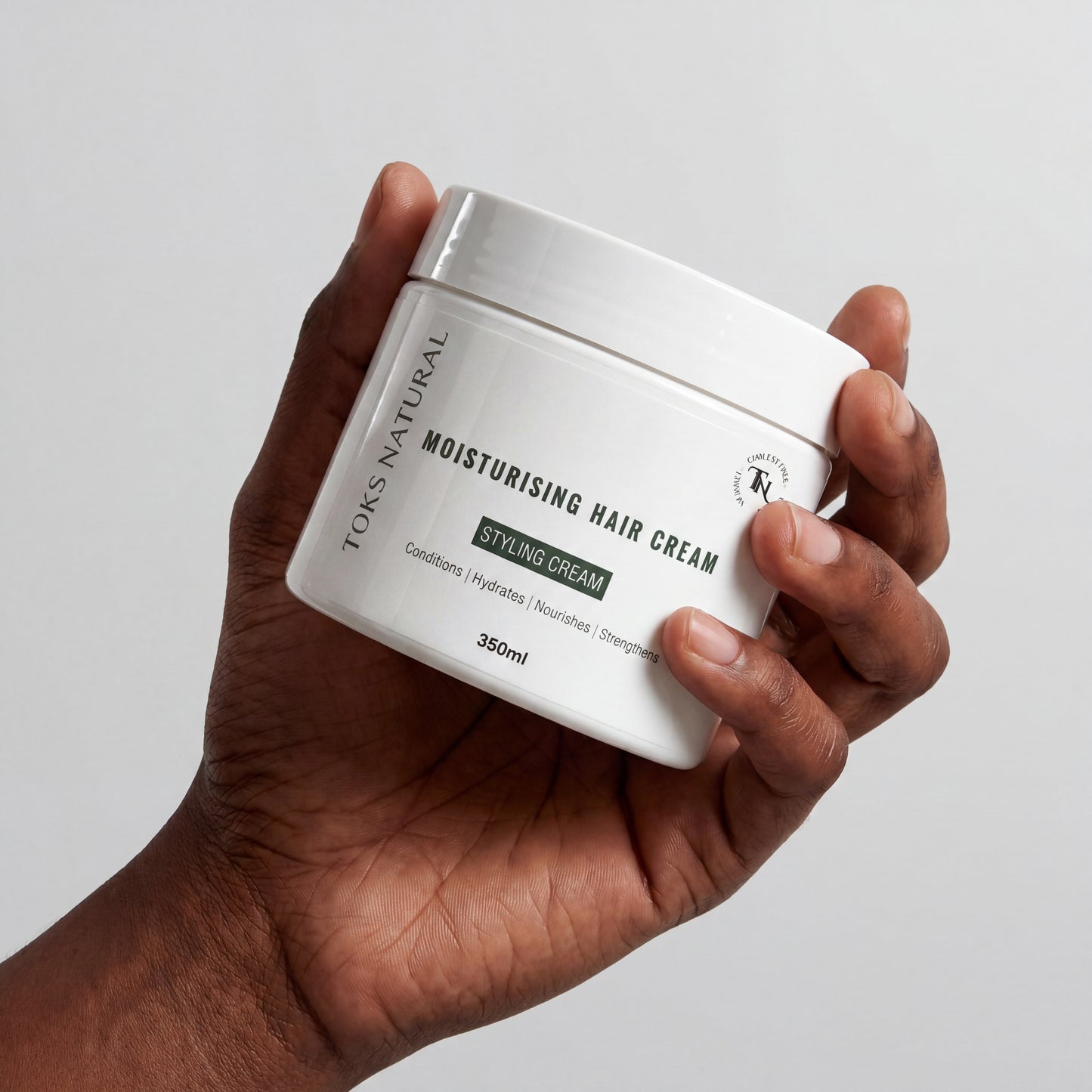 Hand holding a jar of TOKS Natural Moisturising Hair Cream against a plain background