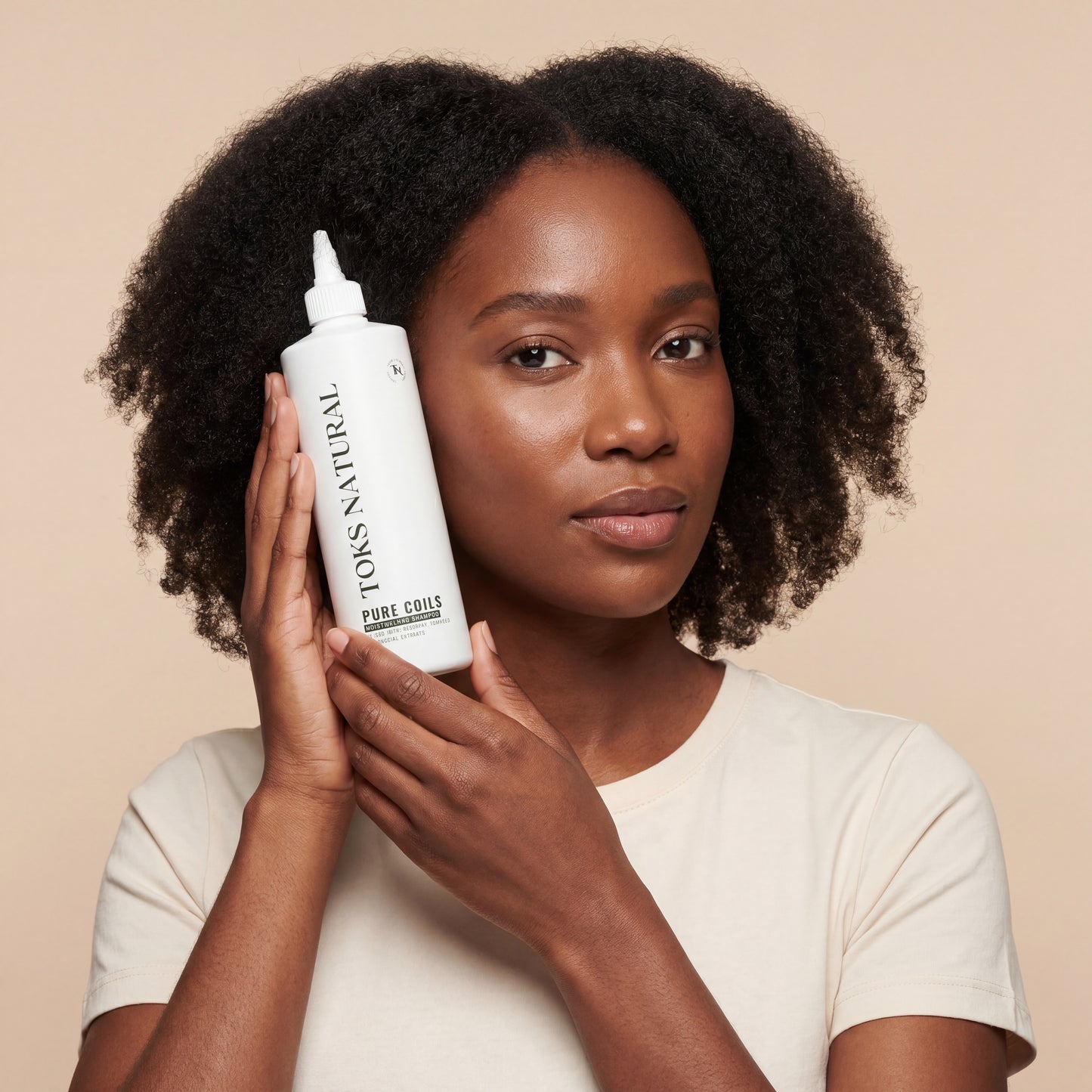 Woman holding a bottle of Toks Natural hair product against a beige background