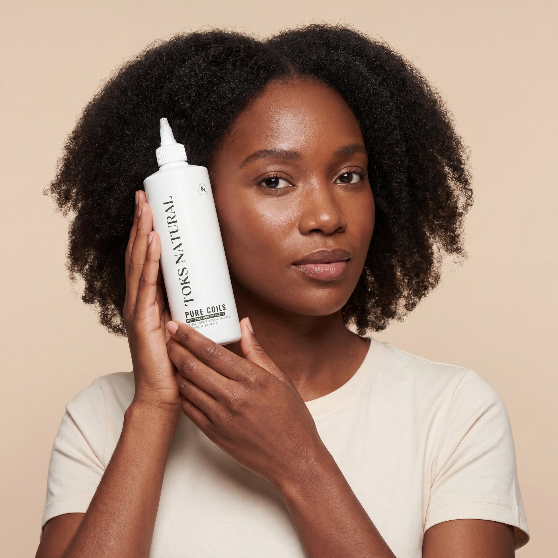 Woman holding a bottle of Toks Natural hair product against a beige background