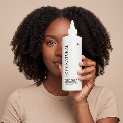 Woman holding a bottle of Toks Natural hair product against a beige background