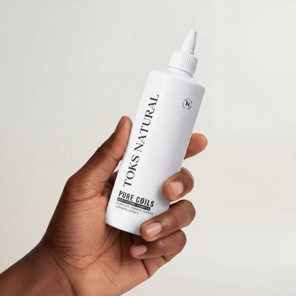 Hand holding a white bottle labeled 'TOKS NATURAL' against a light background