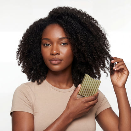 Woman with curly hair holding a green bar of soap against a white background