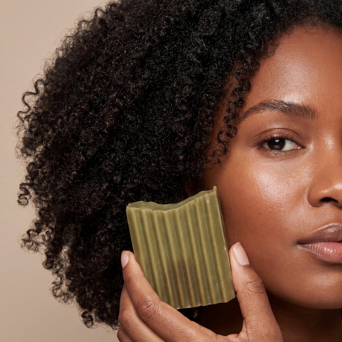 Woman holding a green bar of soap against a beige background