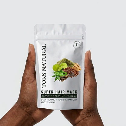 Hand holding a package of Toks Natural Super Hair Mask against a light gray background