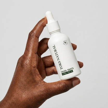 Hand holding a white bottle labeled 'Toks Natural' against a gray background