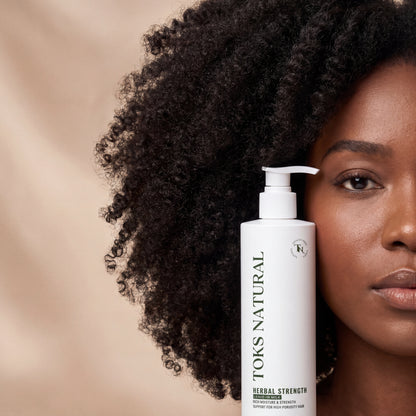 Woman with curly hair holding a bottle of TOKS NATURAL hair product against a beige background