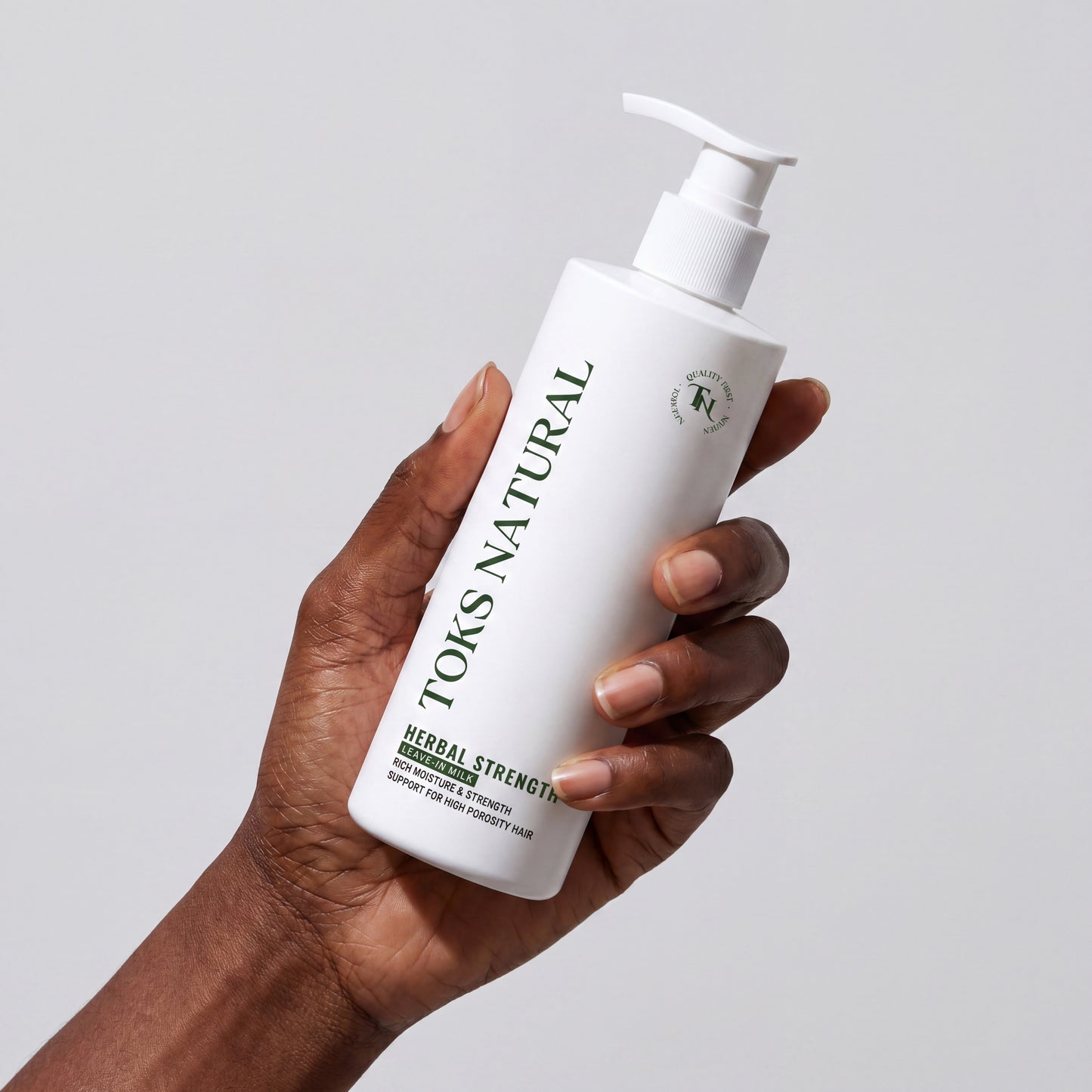 Hand holding a bottle of Toks Natural hair product against a plain background