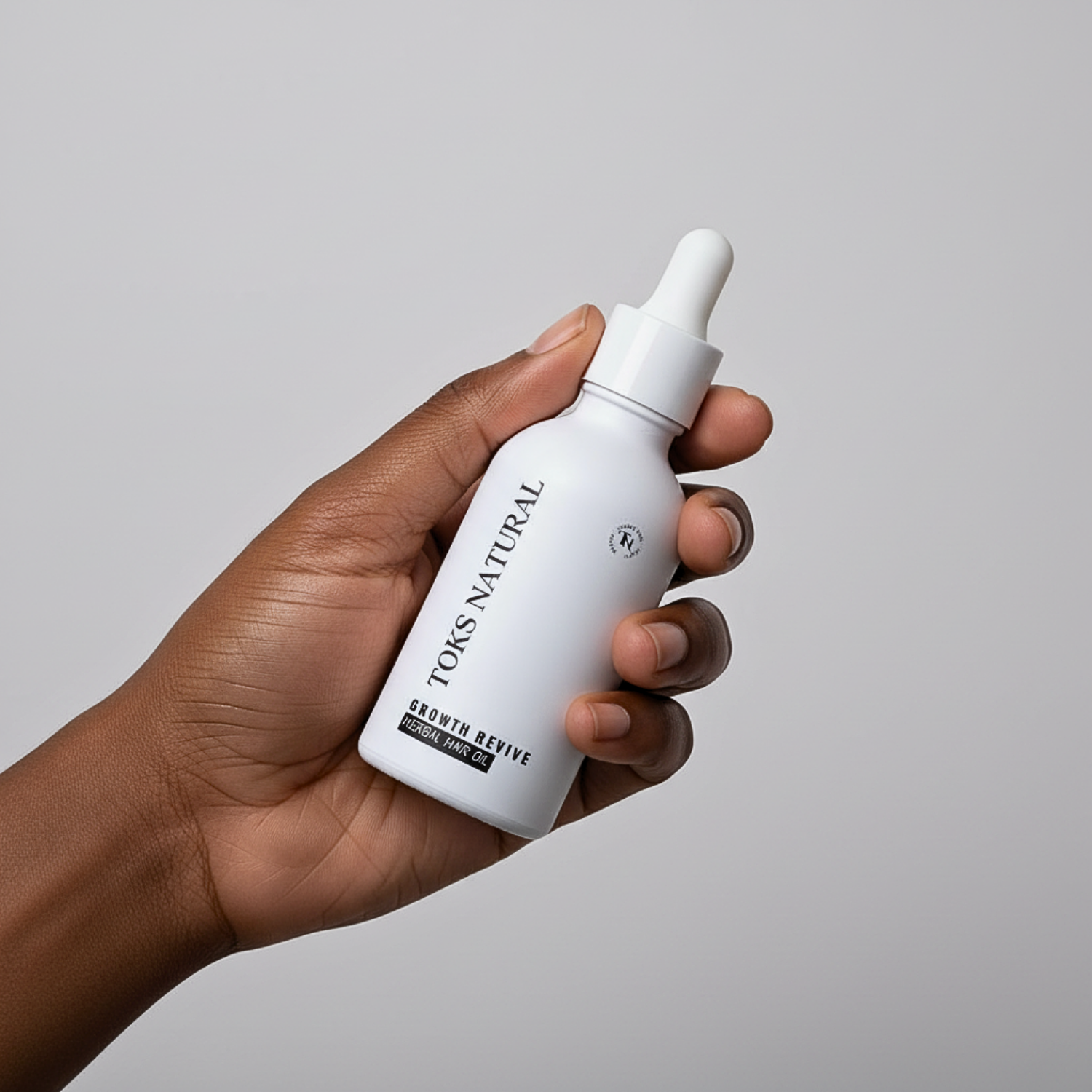 Hand holding a white Toks Natural skincare bottle against a gray background