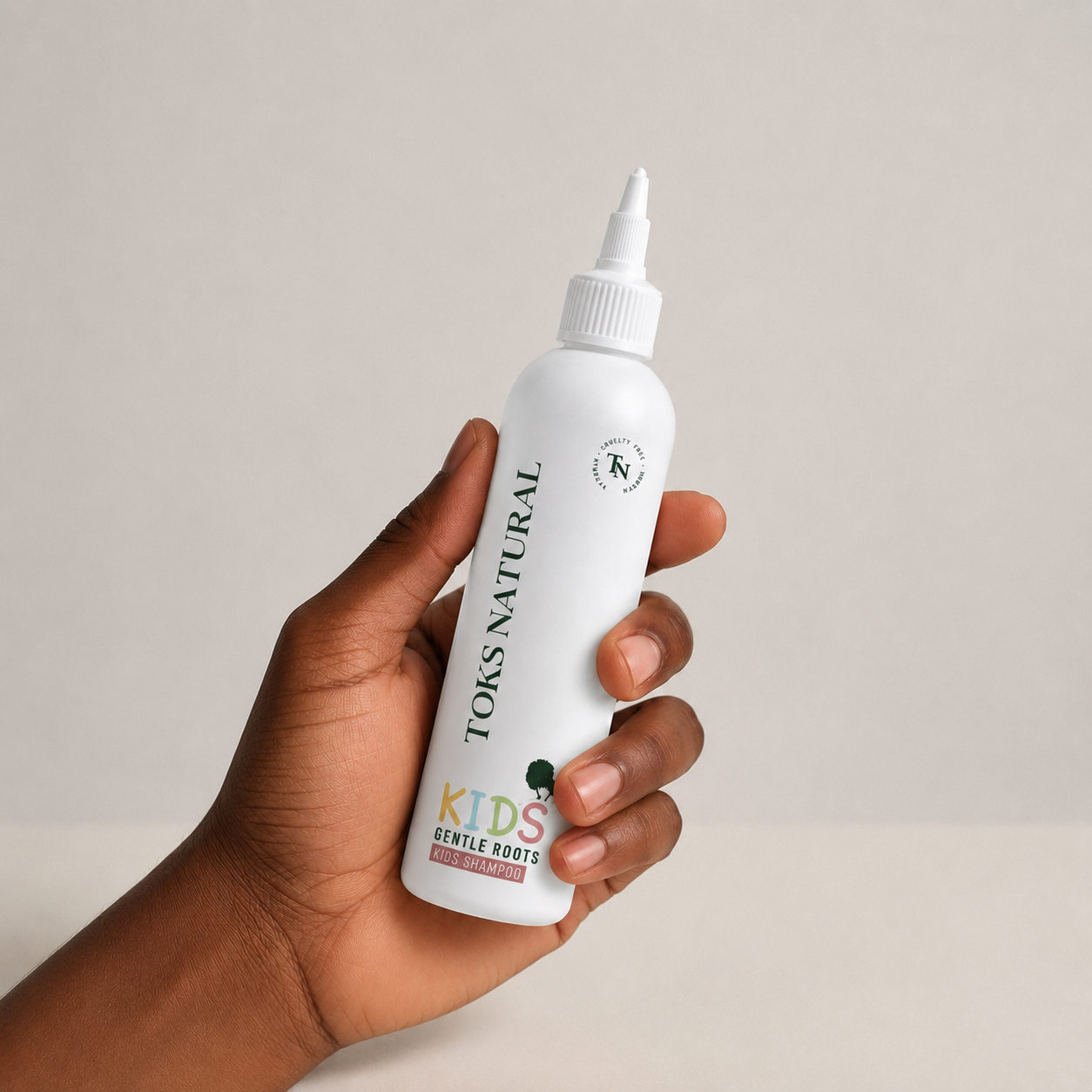 Hand holding a bottle of Toks Natural Kids Gentle Roots product against a neutral background